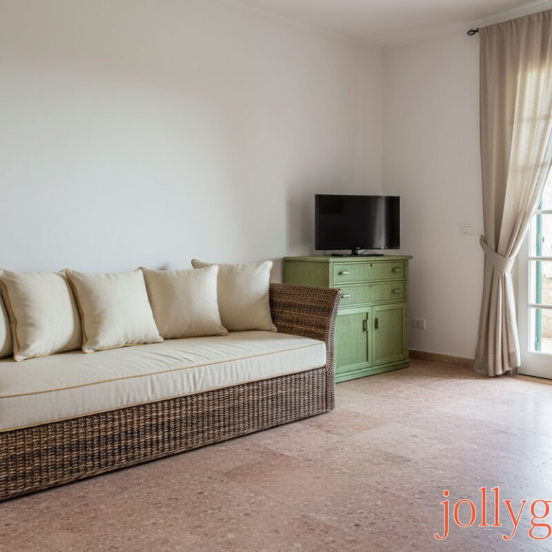 Divano letto in rattan piccolo con cuscini beige, soggiorno luminoso.