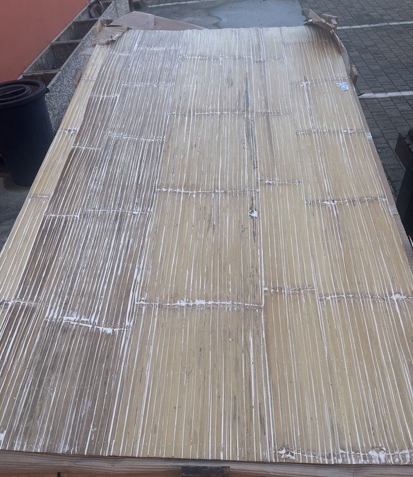 Large stack of rectangular wooden boards wrapped in plastic on a sidewalk outside a building