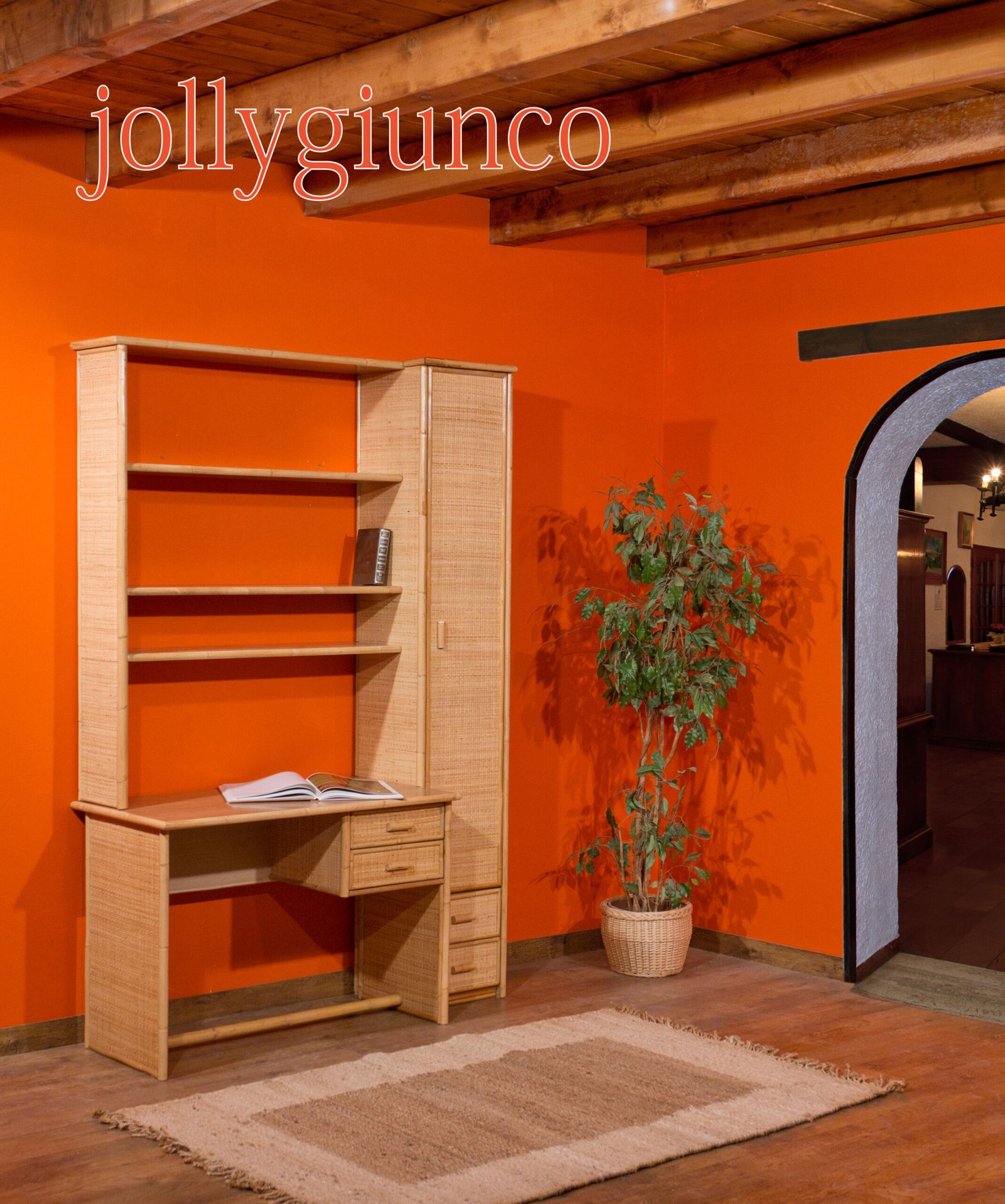 Scrivania Venezia in giunco con libreria 1 jollygiuncoeu wooden desk with open book and tall bookshelf against bright orange wall with a potted plant nearby and wooden ceiling beams above