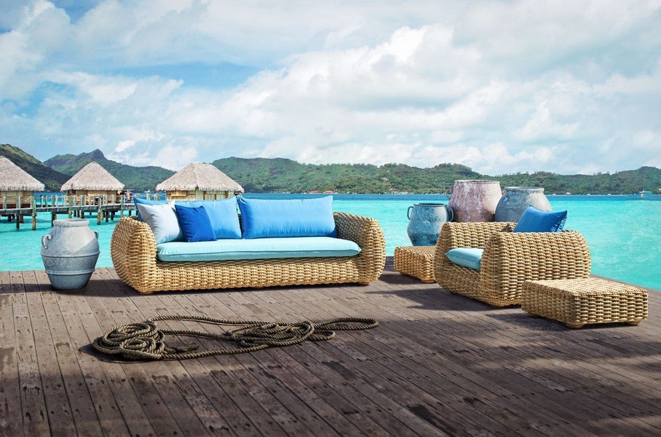 Bombo Divano 3 posti5 jollygiuncoeu wicker outdoor lounge on a wooden deck by turquoise sea with blue cushions and large ceramic pots