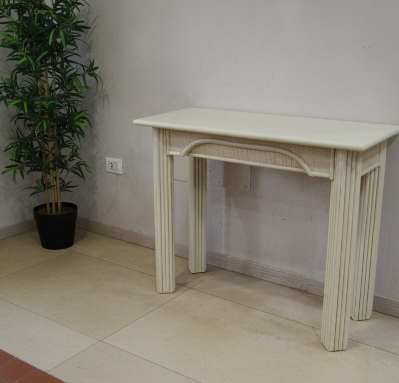 Cream-colored decorative console table with fluted legs in a room corner, beside a tall potted plant and sheer curtains.