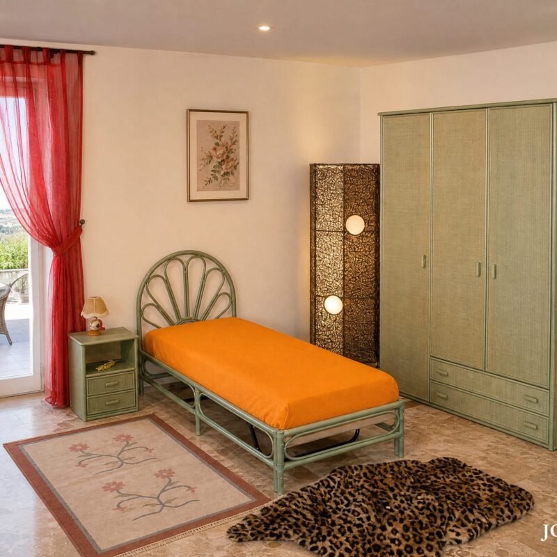 Bedroom with orange bed and green metal frame, tall green wardrobe, and red sheer curtains by a balcony door.