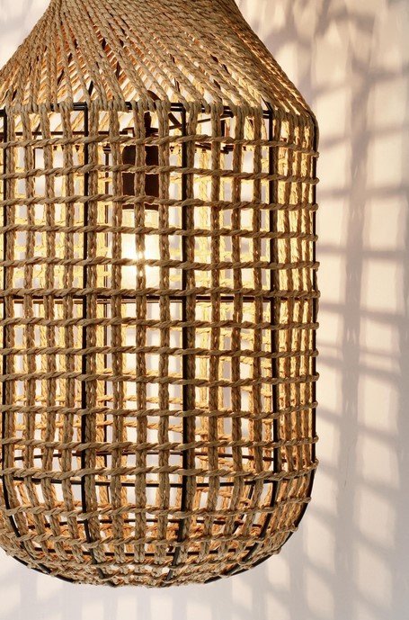 LAMPADARIO MALABO NATURALE H1323 jollygiuncoeu woven rattan pendant lamp with a warm light bulb inside casting lattice shadows on a white wall