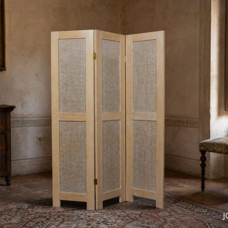 Three-panel woven room divider stands in a vintage parlor, with an antique wooden dresser and a candle on top.