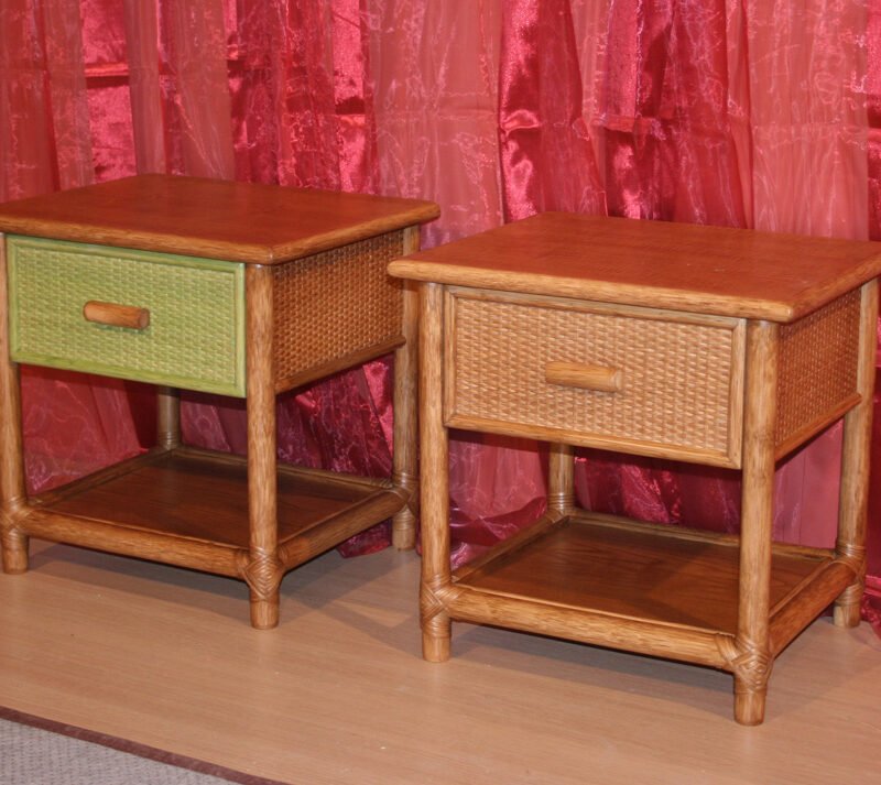 Pair of wooden wicker end tables with drawers (one green) and lower shelves, on a light floor against red draped backdrop.