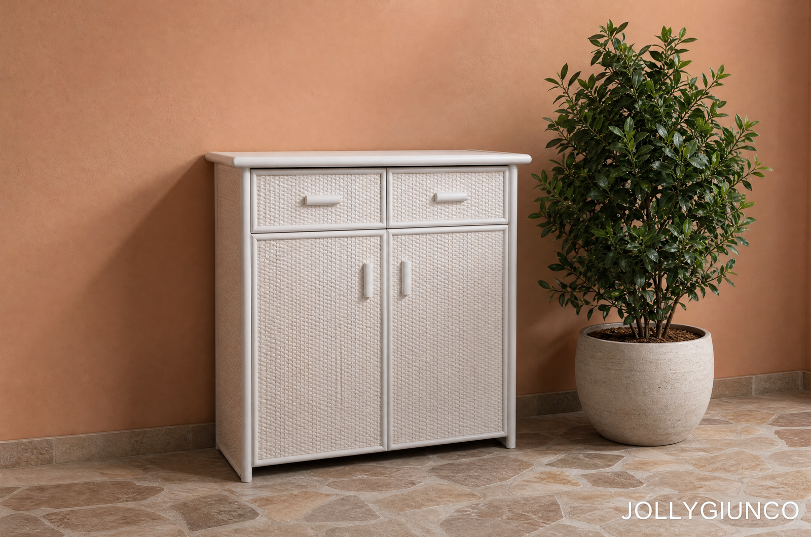 Scarpiera in Rattan 2 Porte e 1 Cassetto jollygiuncoeu white wicker cabinet with four drawers beside a large potted green plant against a peach wall on a tiled floor brand name jollygiunco appears in the corner bottom right