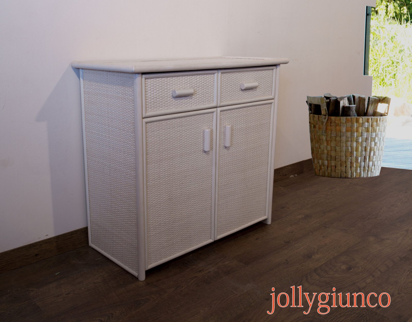 jollygiuncovari40g jollygiuncoeu white wicker dresser with four drawers against a pale wall a woven basket sits on the floor to the right near a doorway with outdoor light