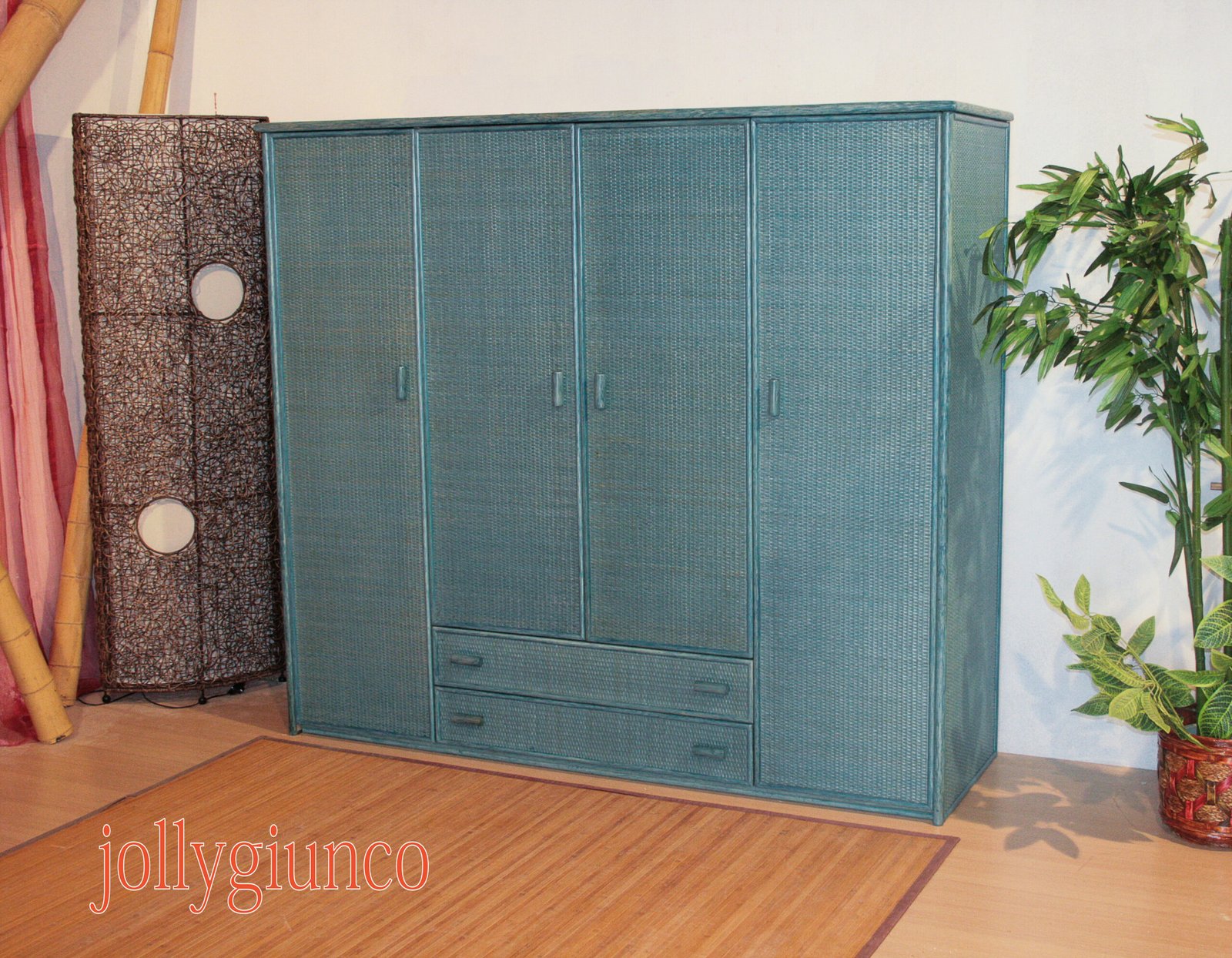 jollygiuncoarmadiorattan32g jollygiuncoeu blue woven storage cabinet with doors and drawers placed in a showroom next to a wicker screen and a potted plant on the right text at the bottom edge partially visible